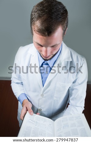 Closeup portrait of handsome young doctor reading over gray background