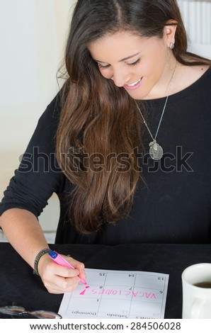 close portait of brunette girl sitting and writing on a paper with head tilted down towards desk with coffee mug, vacation written in Spanish