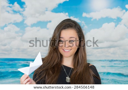 brunette holding an origami paper figure in front of oceanic cloud background while looking at the figure