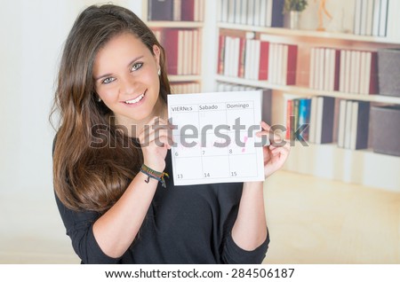 pretty brunette girl holding up a calendar with both hands and smiling to camera, spanish words say friday, saturday, sunday, vacation