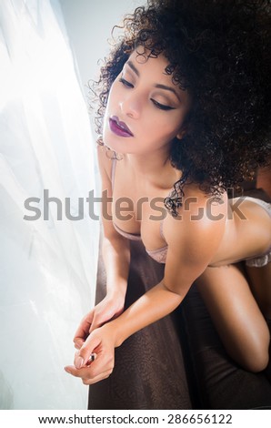 girl sitting on her knees in sofa wearing lingerie with a desirable facial expression