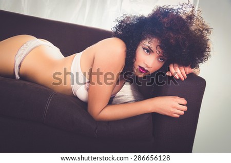 girl posing sensually in sofa wearing lingerie lying on her stomach looking forward