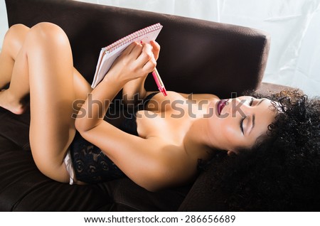 girl wearing lingerie lying on her back in sofa writing with pen and paper