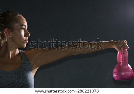 Profile shot of fit womans face and arm holding up a pink weight object