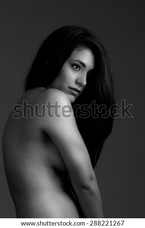 Upper body sideways shot of hispanic model posing nude and covering breasts with arms black and white edition