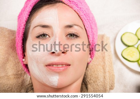 Closeup woman from above angle with white cream covering half of face looking at camera