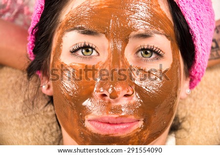 Closeup womans face covered in brown facial treatment cream and looking to camera