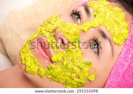 Closeup womans face covered with green cream and eyes open wearing pink towel on head lying down