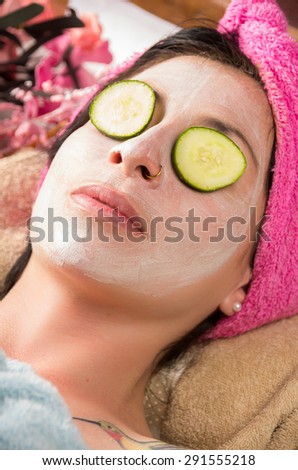 Closeup woman from above angle with white cream on face an cucumber over eyes