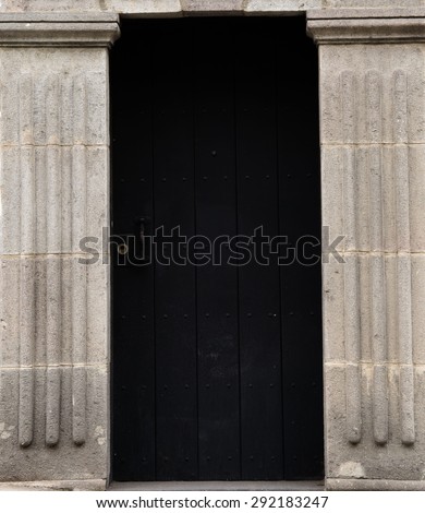 Ancient style entrance with big black wooden door and big cement poles on the both sides