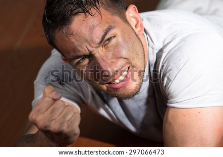Hispanic man with dirty face and shirt lying on floor desperate facial expression making a fist from right hand.