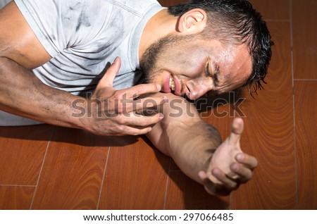 Hispanic man with dirty face and shirt lying on floor left arm reaching towards camera.