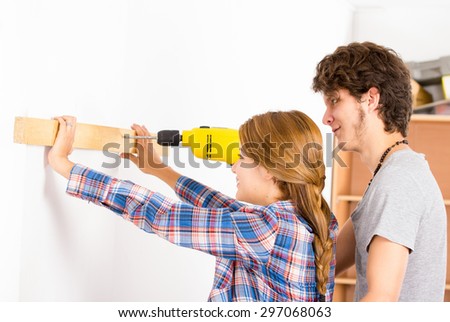 Couple renovating together as man using power drill on wood part and woman helping out by holding.