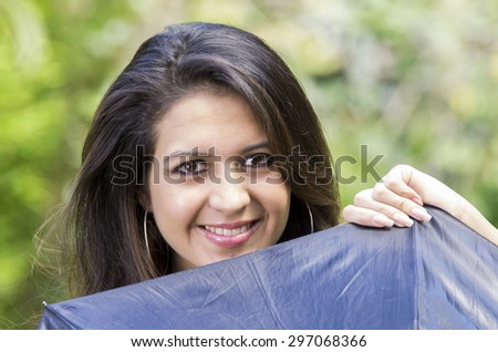 Closeup hispanic brunette model head peeking up from behind black umbrella smiling to camera with beautiful eyes.
