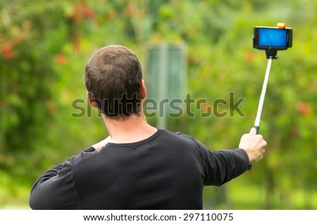Hispanic man posing with selfie stick in park environment, his back facing camera.