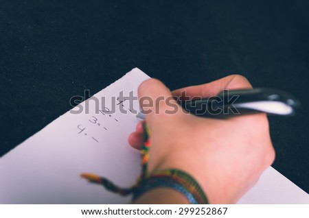 closeup of female right hand with textile bracelet writing on paper with black background