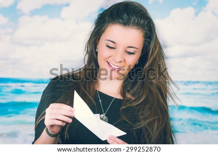 beautiful brunette holding an origami paper figure in front of oceanic cloud background while looking at the figure with sky background