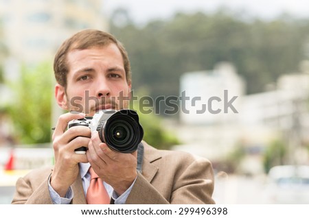 Successful attractive male photographer in brown suit working outdoors in traffic urban environment holding camera.