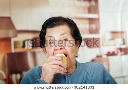 Older hispanic happy woman wearing blue sweater sitting in front of camera having a bite off cupcake.