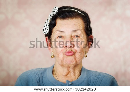 Older cute hispanic woman wearing blue sweater and polka dot bowtie on head making kiss lips for the camera.
