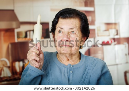 Older cute hispanic woman in blue sweater holding up a rolling pin.