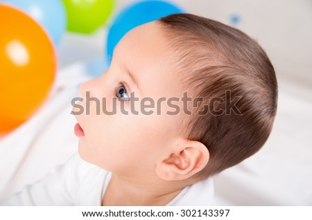 cute surprised baby boy looking left in white background with colorful ballons