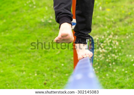 Closeup of mans feet balancing a tightrope or slackline in park environment with one foot above rope.