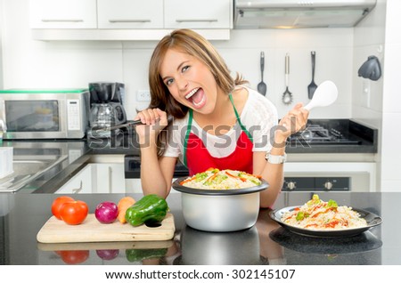 Hispanic beautiful woman cooking in modern kitchen by bench with veggies and pot of food holding a knife out sideways.