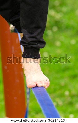 Closeup man feet walking on tightrope or slackline and grassy background.
