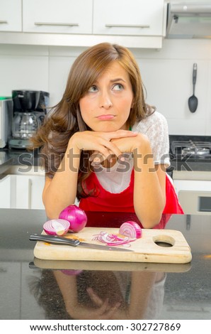 beautiful woman cooking in modern kitchen looking sad with onions on chopping board.