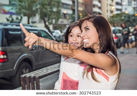 Mom and daughter in urban environment with mother holding girl pointing.