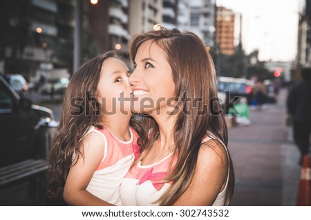 Mom and daughter in urban environment with girl kissing mother on cheek.
