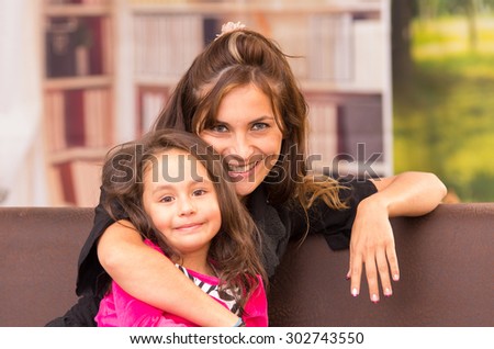 Mom and daughter posing happily indoors in sofa smiling to camera.