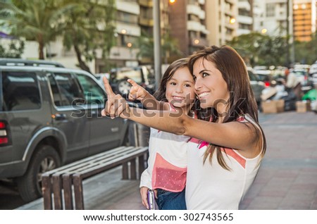 Mom and daughter in urban environment with mother holding girl pointing.