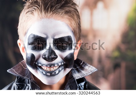 Scary little boy smiling wearing skull makeup for halloween