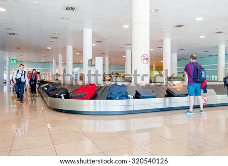 BARCELONA, SPAIN - 8 AUGUST, 2015: Conveyer belt for arrivals luggage with suitcases and people around waiting inside large bright colored hall at airport.