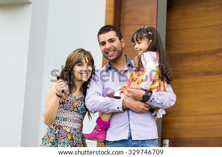 Adorable hispanic family of three posing for camera outside front entrance door.