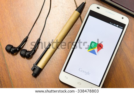 QUITO, ECUADOR - AUGUST 3, 2015: White smartphone lying on desk with Google maps screen open next to a pen and headphones, business communication concept.