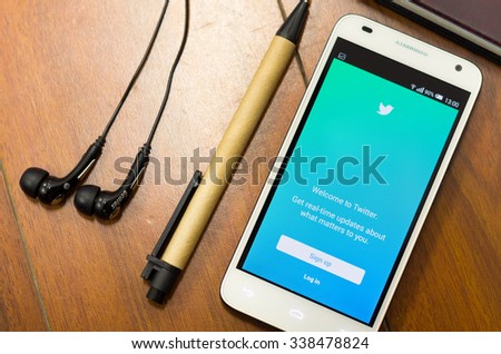 QUITO, ECUADOR - AUGUST 3, 2015: White smartphone lying on desk with Twitter screen open next to a pen and headphones, business communication concept.