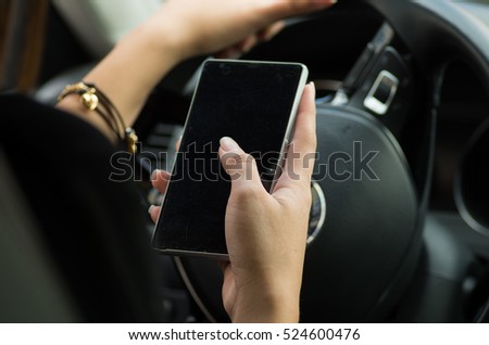 Closeup inside vehicle of hand holding smartphone, steering wheel and black interior background, female driver concept