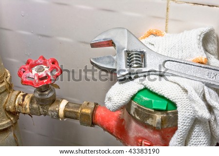 Sanitary equipment still life with old rusty tubes, brass valve with red cap, red and green water meter, white protective cloves and shiny metal wrench.