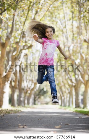 Portrait of Smiling Tween Girl Jumping on Pathway between Trees