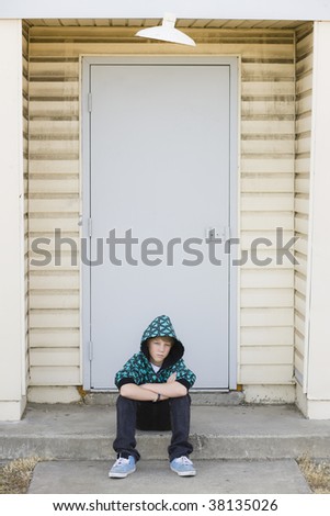 Tween Boy in Hooded Sweatshirt Sitting on a Curb in Front of Door