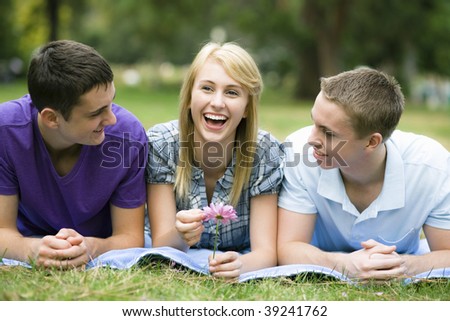 Three Smiling Teens Lying on a Blanket in a Park