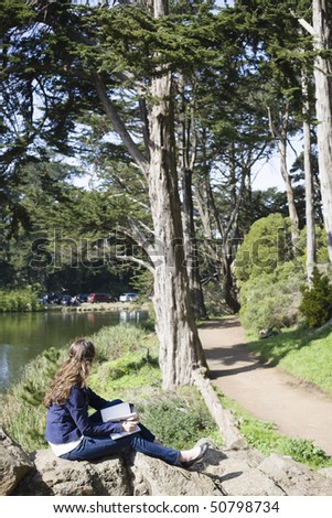 Young Woman Sitting in a Park and Writing in a Journal