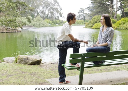 Two Teenagers on a Park Bench By The Water Smiling To Each Other
