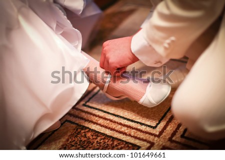 Groom in white costume is helping to wear classic wedding shoes on a bride before start of wedding ceremony.