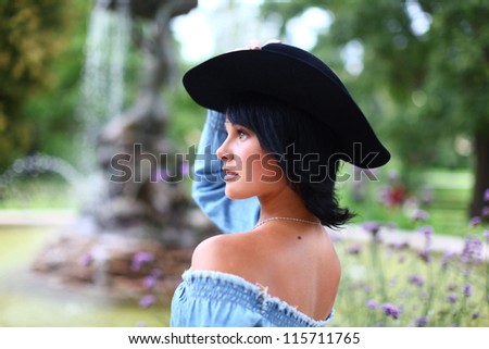 Portrait of young dreaming beautiful girl in country style with cowboy hat in summer park against fountain in Old Riga, Latvia