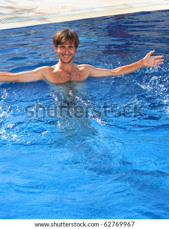 Young man with a big smile on his face in swimming pool with clear blue water