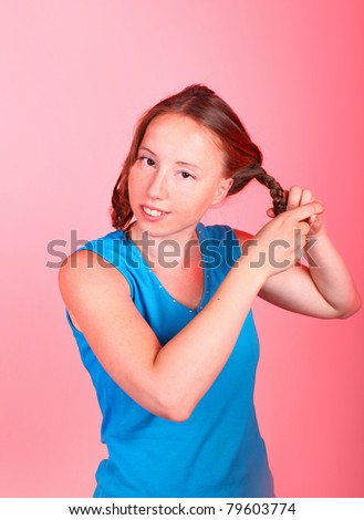 Sweet athletic girl in sporty blue t-shirt is making a hair braids on a red background.